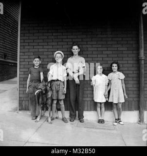 Les enfants du quartier et un chien s'alignent pour une photo contre un mur de briques, ca. 1928. Banque D'Images