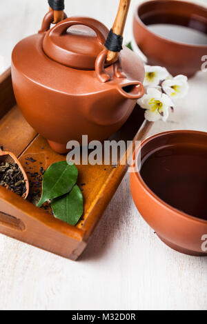 Théière en céramique, les feuilles de thé et sakura sur un plateau en bois, vue du dessus. Thé Oriental. Banque D'Images