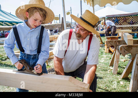 Kutztown Folk Festival, Pennsylvania Dutch folklife Amish, homme garçon père fils, menuisier, avion de bois outil enseignement chapeau de paille portant des bretelles Banque D'Images