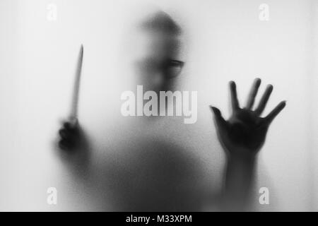 Meurtrier d'horreur. Homme dangereux derrière le verre dépoli avec un couteau à sa main.Halloween.fond noir et blanc photo Banque D'Images