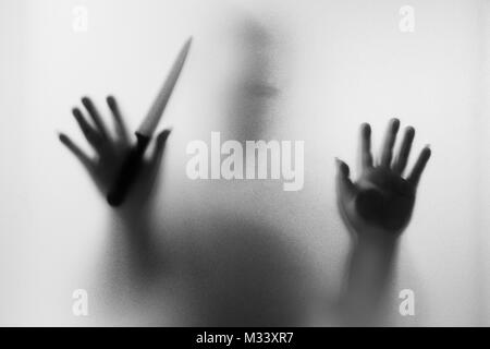 Meurtrier d'horreur. Homme dangereux derrière le verre dépoli avec un couteau à sa main.Halloween.fond noir et blanc photo Banque D'Images