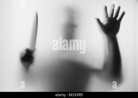Meurtrier d'horreur. Homme dangereux derrière le verre dépoli avec un couteau à sa main.Halloween.fond noir et blanc photo Banque D'Images