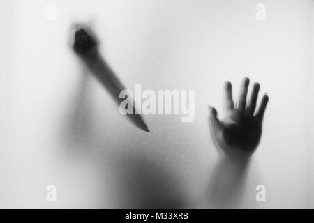 Meurtrier d'horreur. Homme dangereux derrière le verre dépoli avec un couteau à sa main.Halloween.fond noir et blanc photo Banque D'Images