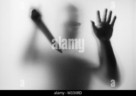 Meurtrier d'horreur. Homme dangereux derrière le verre dépoli avec un couteau à sa main.Halloween.fond noir et blanc photo Banque D'Images