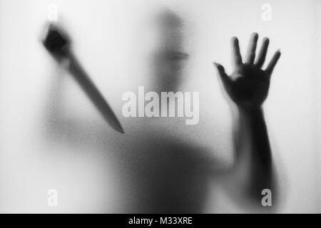 Meurtrier d'horreur. Homme dangereux derrière le verre dépoli avec un couteau à sa main.Halloween.fond noir et blanc photo Banque D'Images