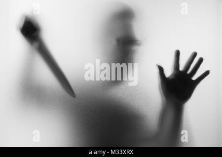 Meurtrier d'horreur. Homme dangereux derrière le verre dépoli avec un couteau à sa main.Halloween.fond noir et blanc photo Banque D'Images