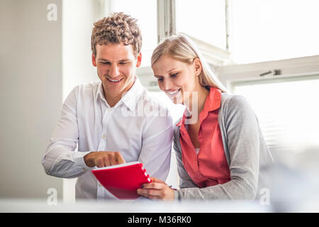 Smiling young business people looking at annexes dans diary at office Banque D'Images