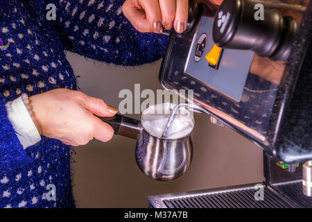 La main de femme tenant une cruche de lait en acier inoxydable d'écume, sous la baguette de vapeur vapeur / une machine à expresso commerciale, de créer de la mousse. UK. Banque D'Images