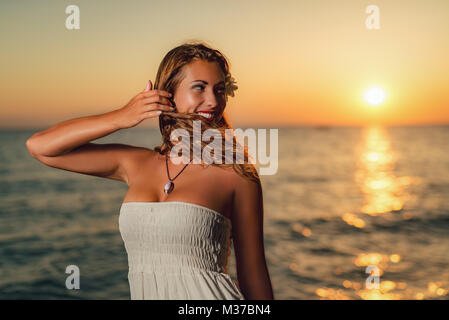 Portrait d'une jolie jeune femme en robe blanche appréciant le coucher du soleil sur la plage. Banque D'Images