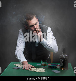 Un gars dur gangster fume un cigare et boit du whisky à la table de poker Banque D'Images