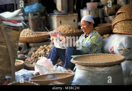 Le Vietnam. Hanoi. Vieux quartier. Vendeur de pommes de terre, femme, lecture, magazine dans sa boutique. Banque D'Images