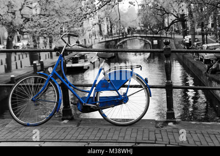 Une photo d'un seul vélo bleu sur le pont sur le canal à Amsterdam. Le fond est noir et blanc. Banque D'Images