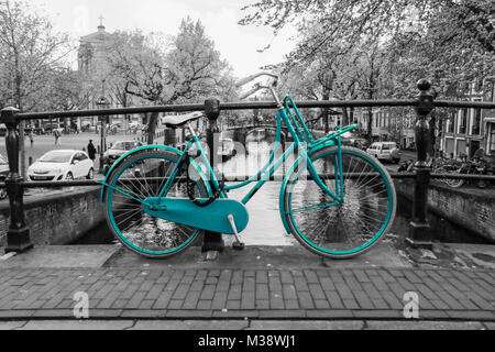 Une photo d'un seul d'azur à vélo sur le pont sur le canal à Amsterdam. Le fond est noir et blanc. Banque D'Images