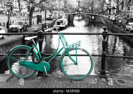 Une photo d'un seul d'azur à vélo sur le pont sur le canal à Amsterdam. Le fond est noir et blanc. Banque D'Images