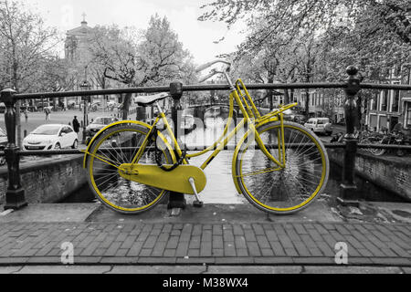 Photo d'un vélo jaune solitaire sur le pont au-dessus du canal d'Amsterdam. L'arrière-plan est noir et blanc. Banque D'Images