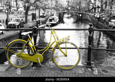 Photo d'un vélo jaune solitaire sur le pont au-dessus du canal d'Amsterdam. L'arrière-plan est noir et blanc. Banque D'Images