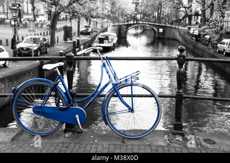 Une photo d'un seul vélo bleu sur le pont sur le canal à Amsterdam. Le fond est noir et blanc. Banque D'Images
