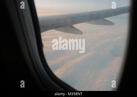 Nuages et ciel vu à travers la vitre d'un aéronef au coucher du soleil Banque D'Images