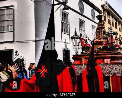 Tourné à contraste élevé de pénitents en cagoules noires dans la Semaine Sainte (Semana Santa) procession, La Laguna, Tenerife, Canaries marcher de l'avant du flotteur Banque D'Images