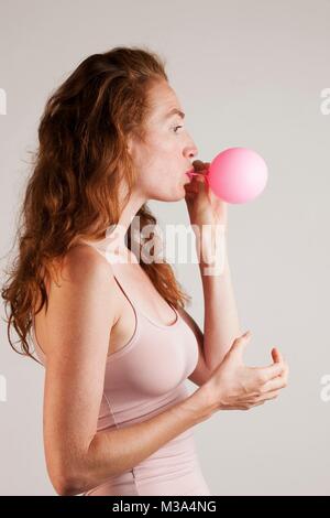 Parution du modèle. Profil de jeune femme aux cheveux rouges l'explosion ballon rose. Banque D'Images