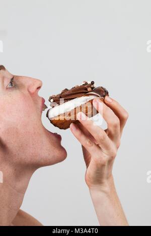 Parution du modèle. Close-up profile of woman eating chocolate donut. Banque D'Images