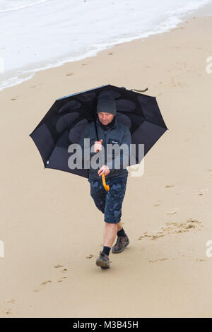 Bournemouth, Dorset, UK. 10 Février, 2018. Météo France : un vent humide jour misérable à Bournemouth - gens luttent avec leurs parasols sur la plage en essayant de rester au sec ! Homme marchant le long littoral holding umbrella. Credit : Carolyn Jenkins/Alamy Live News Banque D'Images