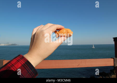 Main tenant une mini gaufre en forme de poisson avec de la crème anglaise le remplissage avec la mer en arrière-plan journée ensoleillée, Corée du Sud Banque D'Images