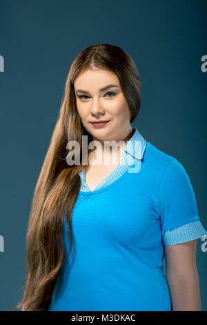 De taille plus attractive woman wearing blue blouse en studio. Fille avec de longs cheveux sur fond bleu. Essai sur modèle Banque D'Images