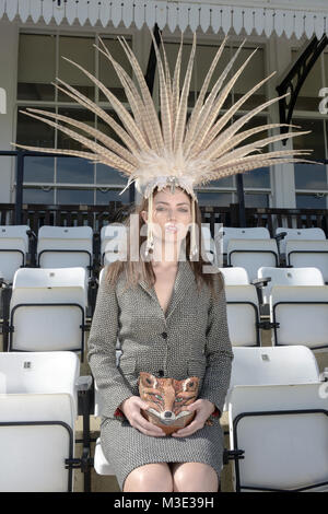 Belle jeune fille portant une robe et une tête spectaculaire costume sur mesure se trouve dans la cale à un Cricket Ground- elle a un sac à main Fox Banque D'Images