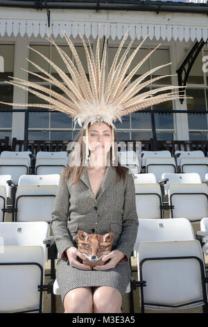 Belle jeune fille portant une robe et une tête spectaculaire costume sur mesure se trouve dans la cale à un Cricket Ground- elle a un sac à main Fox Banque D'Images