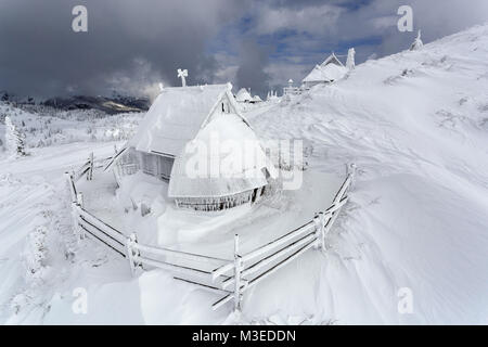 Vue aérienne de gelé et recouvert de neige chalet en bois sur un jour nuageux, Velika Planina, la Slovénie. Banque D'Images