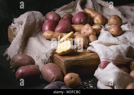 Variété de matières organiques non cuits pommes de différents types et couleurs rouge, jaune, violet sur planche à découper en bois avec cuisine serviettes sur le tableau noir. D Banque D'Images