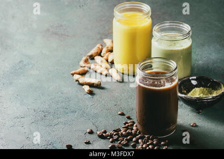 Variété de boissons latte colorés glacés. Le café glacé, le curcuma et le matcha latte cocktails dans des bocaux en verre avec des ingrédients ci-dessus plus de texture gris vert b Banque D'Images