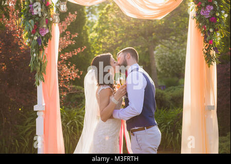 L'époux et épouse ont un baiser au cours de leur cérémonie de mariage dans le jardin Banque D'Images