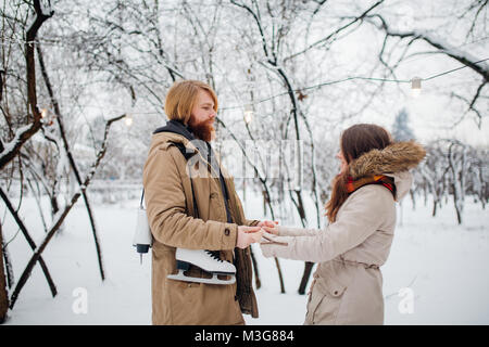 L'hiver et date. Jeune couple amoureux, l'homme et la femme en hiver sur un fond de neige et de la forêt se tenant la main et sourit. Un gars aux cheveux longs et un Banque D'Images