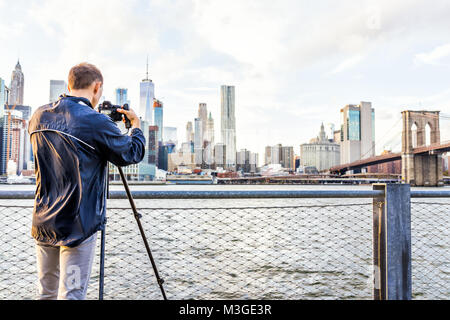 Dos de jeune homme photographe avec appareil photo, trépied, mise en place à l'extérieur extérieur dans NYC New York City Pont de Brooklyn Park par East River, balustrade, looki Banque D'Images