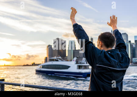 Dos de jeune homme à l'extérieur extérieur dans NYC New York City Pont de Brooklyn Park par East River, garde-corps, à la vue des toits de la ville au coucher du soleil, stat Banque D'Images