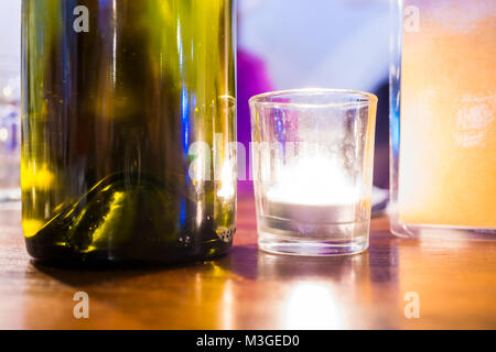 Gros plan macro vue du niveau de la surface du sol petit blanc brillant la lumière de bougie dans le sol en bois table en verre vert bouteille vin romantique réglage dar Banque D'Images