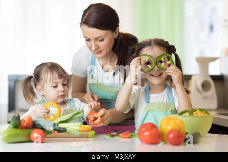 Maman enseigne deux filles à cuisiner à la table de la cuisine avec des aliments crus Banque D'Images