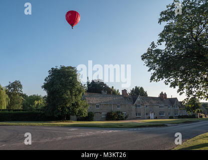 Une Vierge hot air balloon vole à basse altitude au-dessus d'un village du Warwickshire à la recherche d'une place à la terre. UK. Banque D'Images