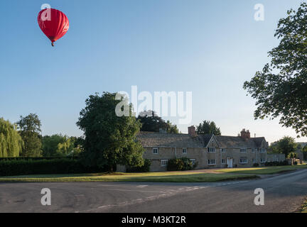 Une Vierge hot air balloon vole à basse altitude au-dessus d'un village du Warwickshire à la recherche d'une place à la terre. UK. Banque D'Images