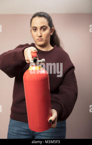 Jeune femme faisant un extincteur rouge vers la caméra avec un air sérieux et se concentrer à la bouteille Banque D'Images