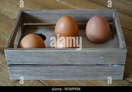 Quatre œufs dans une boîte en bois avec espace pour six oeufs, dans la lumière de la fenêtre. Banque D'Images