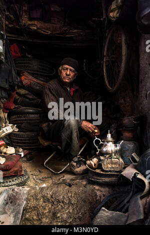 Marrakech,Maroc - Janvier 2018 : l'homme local dans l'atelier obscur de la rue ayant pause thé dans de mauvaises conditions, à Marrakech. Banque D'Images