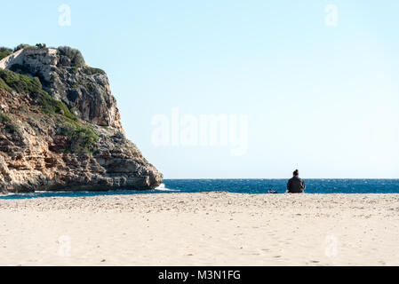 Silhouette d'une femme assise sur le sable de la plage face à la mer méditerranée à Cala Romantica sur l'île de Majorque, Espagne. Banque D'Images