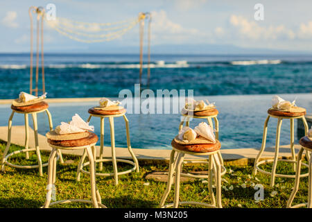 Cérémonie de mariage près de l'océan au coucher du soleil - des chaises pour les clients avec des pétales de fleurs et des fans de bambou et d'une arche de mariage Banque D'Images