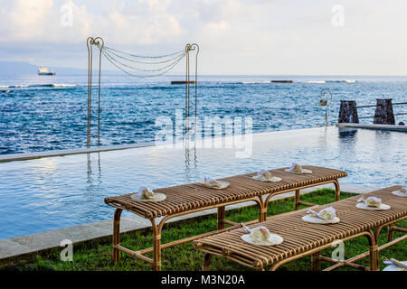 Cérémonie de mariage près de l'océan au coucher du soleil - rotin bancs pour les clients de pétales de fleurs et des fans de bambou, et une arche de mariage Banque D'Images