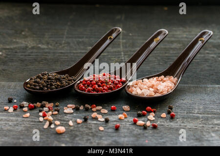 Portrait de trois cuillères à soupe de sel rose, noir et de poivre rose foncé sur fond de bois Banque D'Images