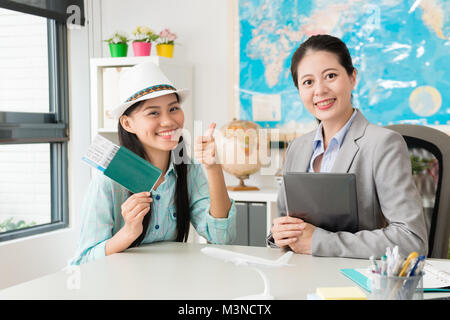 Happy pretty girl holding passport voyageur client avec billet d'avion indiquant thumb up geste et assis en compagnie d'agent de voyages avec les entreprises ne Banque D'Images