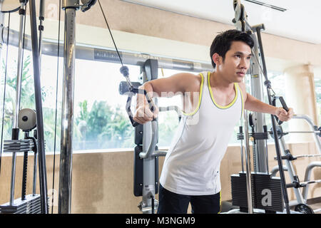 Faible angle de vue portrait d'un bel homme asiatique à la concentration avec le bas tout en exerçant un cable crossover de muscles de coffre dans la salle de sport Banque D'Images
